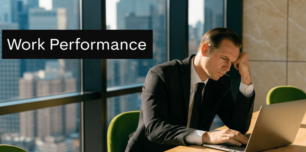 A stressed businessman in a suit working on a laptop in an office overlooking the city